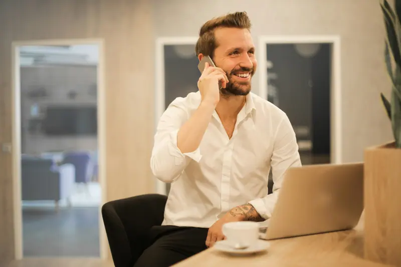 Smiling business owner taking a phone call at his laptop