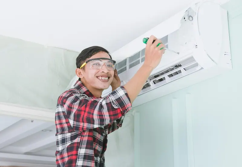 Smiling HVAC technician servicing a wall-mounted air conditioner